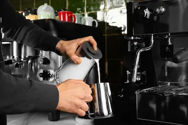 Barista steaming milk behind a shiny, modern espresso machine at Krispy Kreme café.
